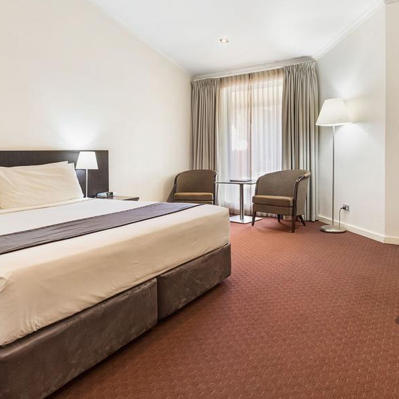 A room at the Karratha International Hotel which includes a king-size bed, chairs and a side table by the window