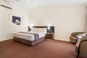 A room at the Karratha International Hotel which features a queen-size bed, two bedside tables with lamps, and a blue and white abstract artwork hung on the wall