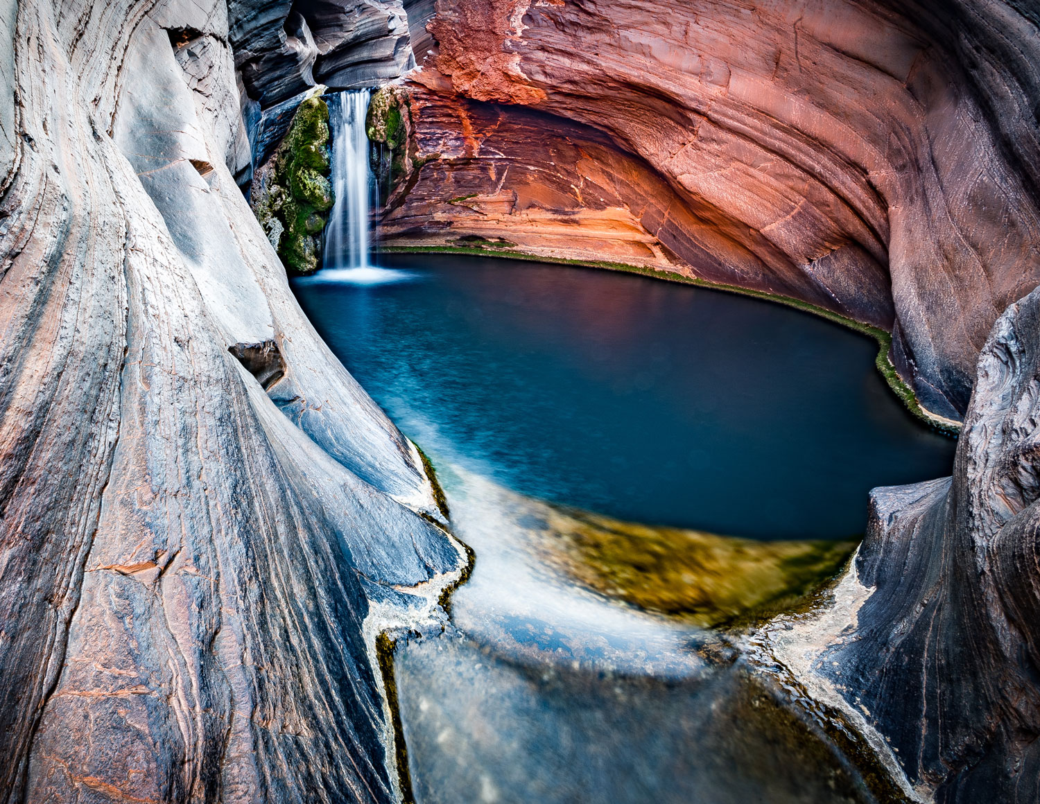 A waterfall fills a small pool inside a rocky area of gorges at Karijini National Park