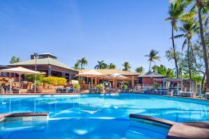 The pool at the Karratha International Hotel is large, outdoors, and surrounded by palm trees and umbrella shades
