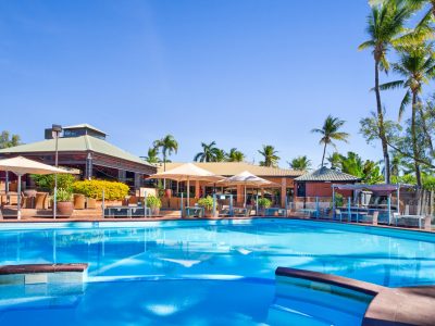 The pool at the Karratha International Hotel is large, outdoors, and surrounded by palm trees and umbrella shades