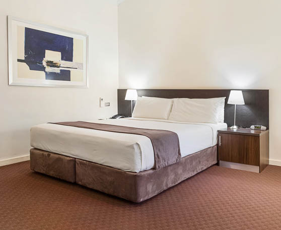 A room at the Karratha International Hotel which features a queen-size bed, two bedside tables with lamps, and a blue and white abstract artwork hung on the wall