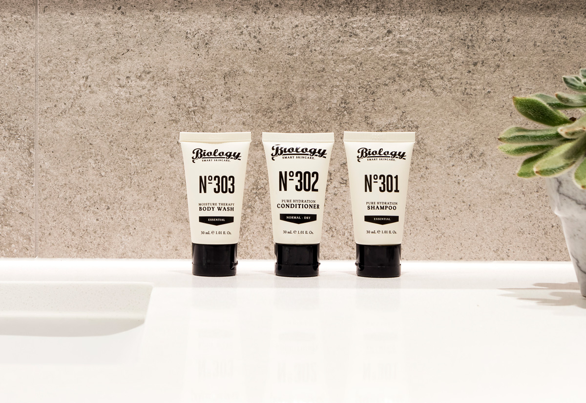 Bottles of body wash, conditioner, and shampoo are neatly arranged on the side of a bathtub