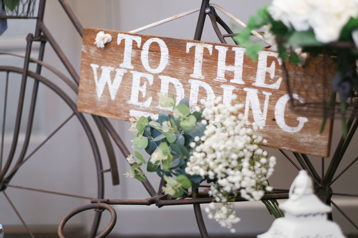 A sign decorated with flowers directs guests to a wedding event