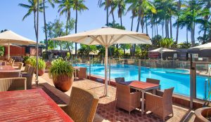 An outdoor table with chairs and an umbrella shade are positioned next to the outdoor pool at the Karratha International Hotel