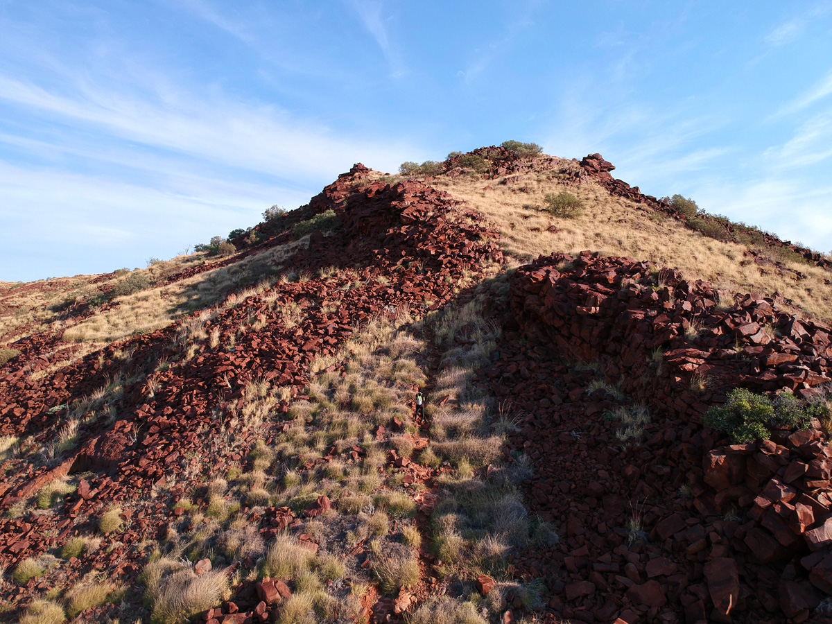 A rocky hill covered with dark red rocks and grassy shrubs