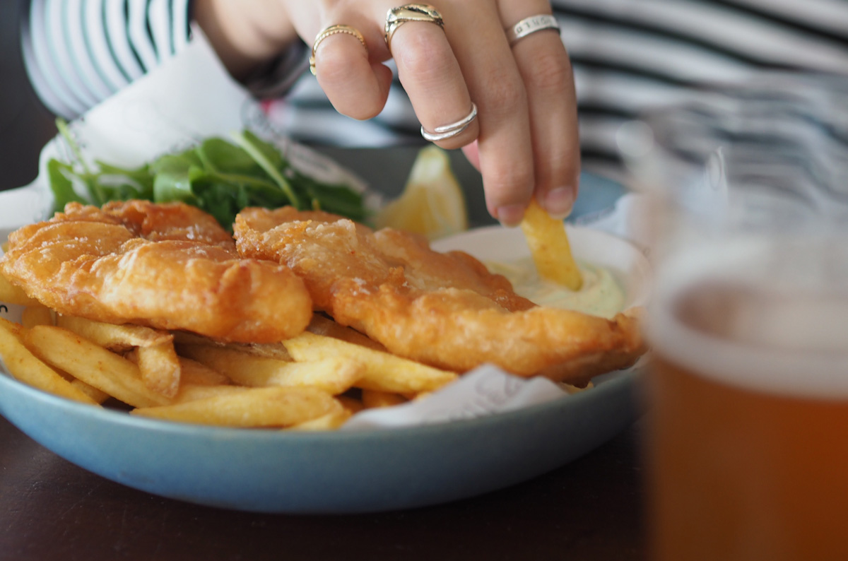 A restaurant guest enjoys a plate of fish and chips served with salad and aioli