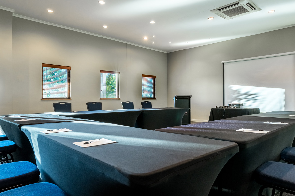 The Goldfinch Conference Room is equipped with conference tables, chairs, water carafes and glasses, a projector, and writing stationery