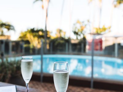 Two glasses of champagne are waiting on a table with a view of the hotel pool and palm trees