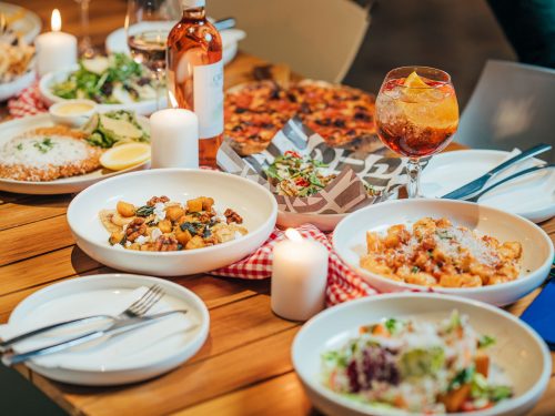 A table holds various dishes of Italian food, including gnocchi pasta, pizza, and salad