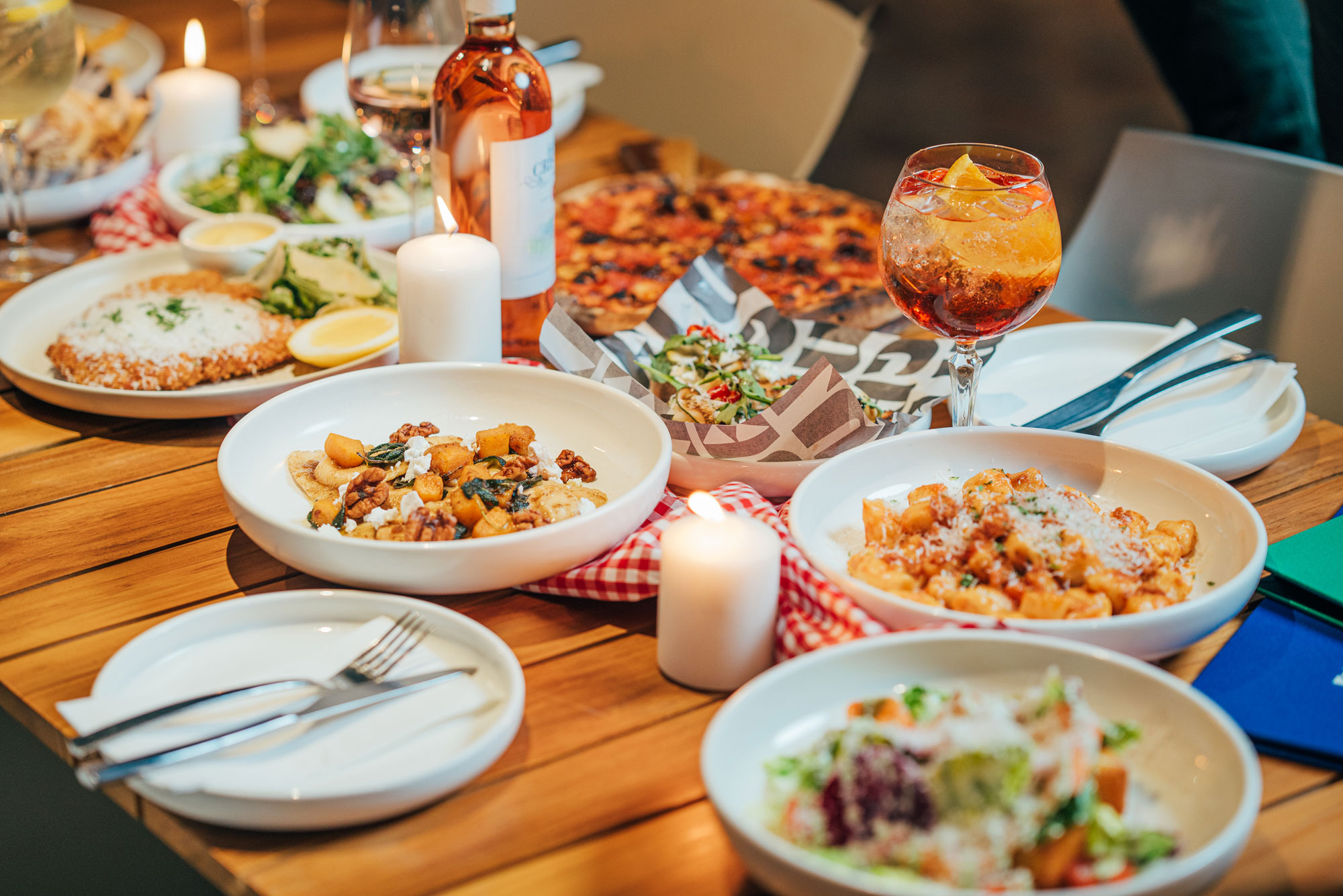 A table holds various dishes of Italian food, including gnocchi pasta, pizza, and salad