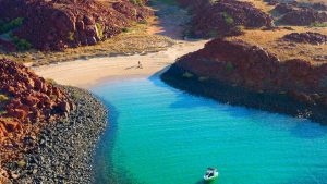 A beach in Karratha with bright blue water, bordered by red rocky hills
