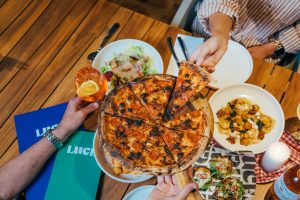 Three restaurant guests share a pizza and enjoy cocktails at Luce Bar e Cibo