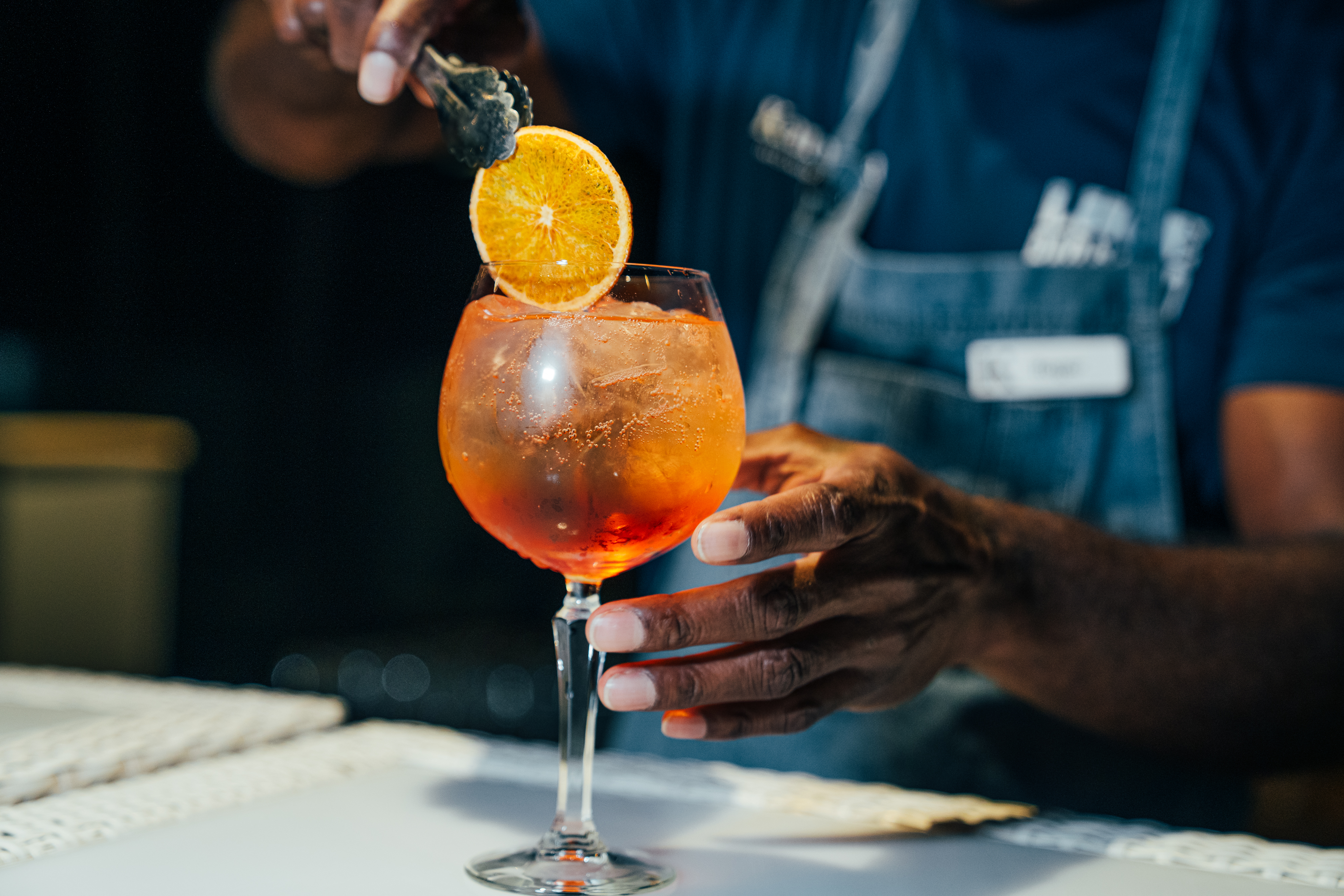 A bartender places a slice of orange inside a glass of Aperol Spritz